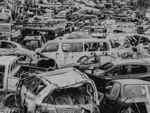 Melnbalts kadrs ar lielu automašīnu kapsētu vai metāllūžņu laukumu, kurā cieši sakrauti simtiem sadragātu, vecu un norakstītu transportlīdzekļu.