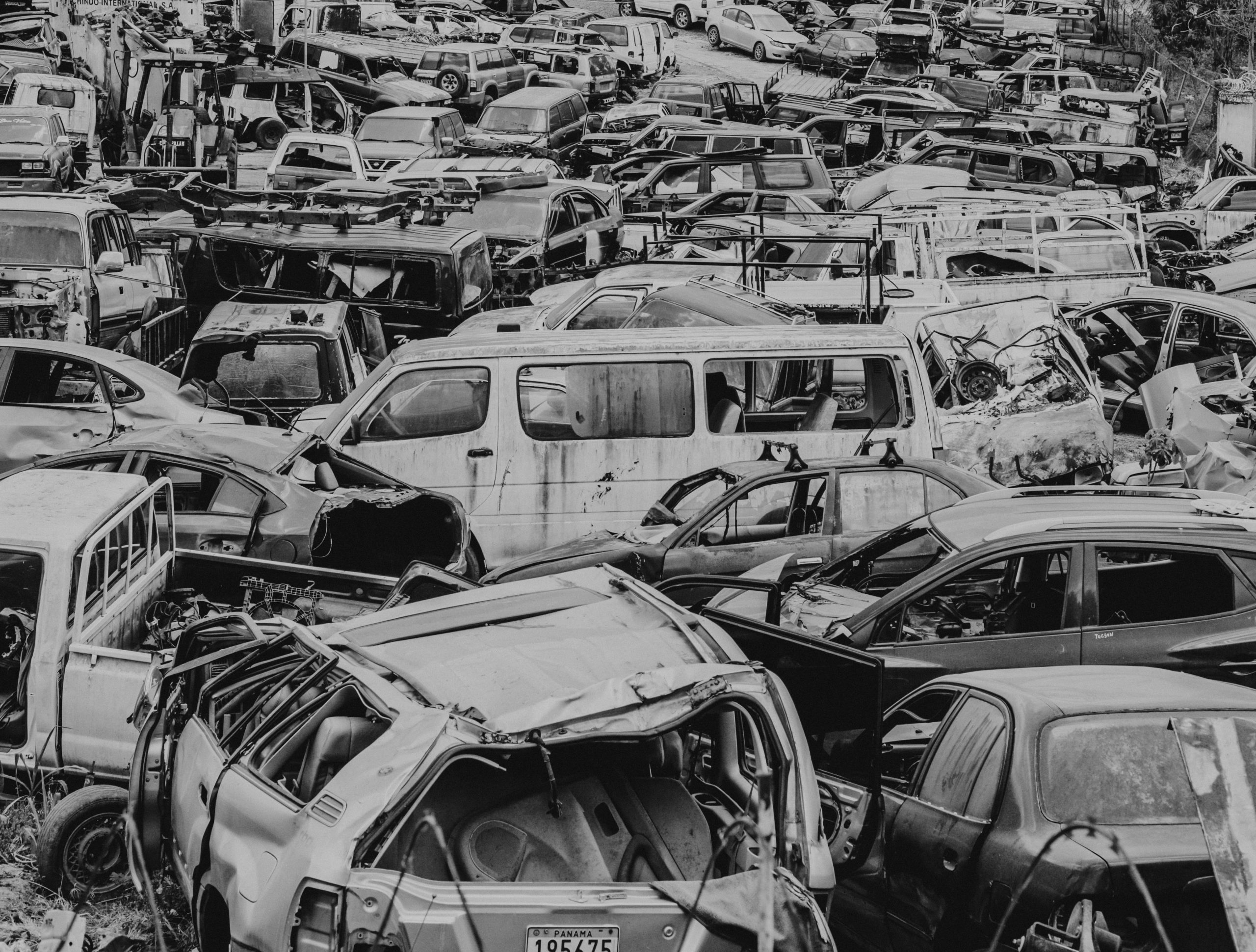 Melnbalts kadrs ar lielu automašīnu kapsētu vai metāllūžņu laukumu, kurā cieši sakrauti simtiem sadragātu, vecu un norakstītu transportlīdzekļu.