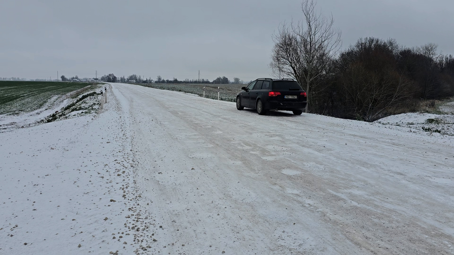 Ziemā piesalis grants ceļš Bauskas novadā ar ceļa malā novietotu automašīnu.