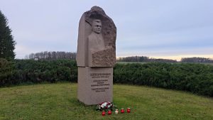 Kārļa Ulmaņa piemiņas piemineklis ar ziediem un svecēm pie tā.