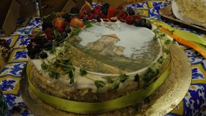 Torte ar fotodruku, kurā attēlotas Viduslaiku pilsdrupas, dekorēta ar ogām un zaļumiem.