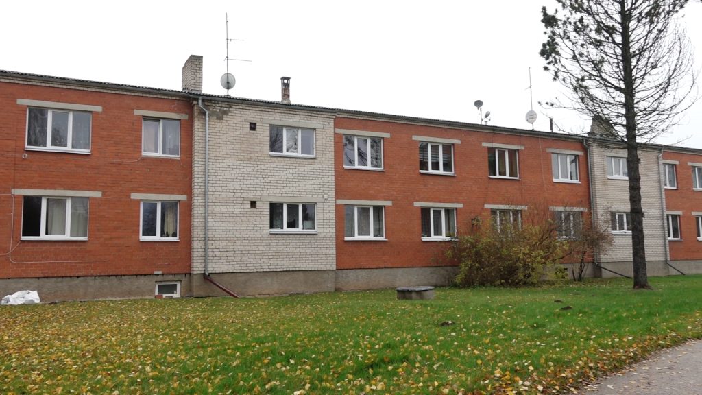 Divstāvu daudzdzīvokļu ēka ar sarkanu un gaišu ķieģeļu fasādi.
