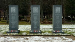 Trīs pieminekļi brīvības cīnītājiem ar svecītēm to pakājē kapsētā ziemas laikā.