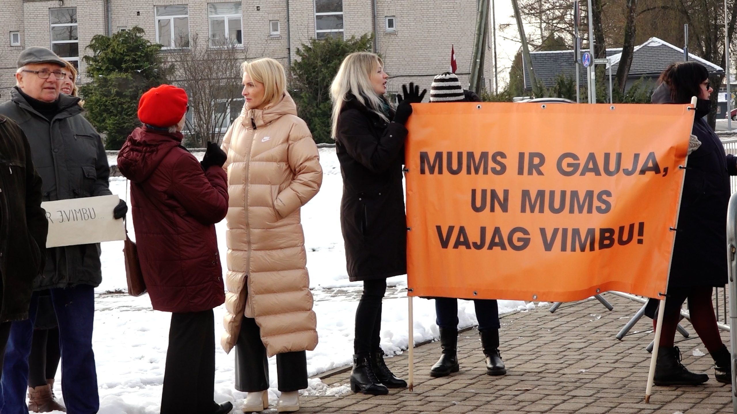 Cilvēki piketā pie Siguldas novada domes, turot oranžu plakātu ar uzrakstu 