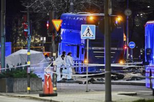 Stokholmas centrā naktī pēc negadījuma. Tumsā redzams tumši zils divstāvu autobuss ar ieslēgtām avārijas gaismām, kuru ieskauj policijas norobežojumi un glābšanas dienestu darbinieki baltos aizsargtērpos.