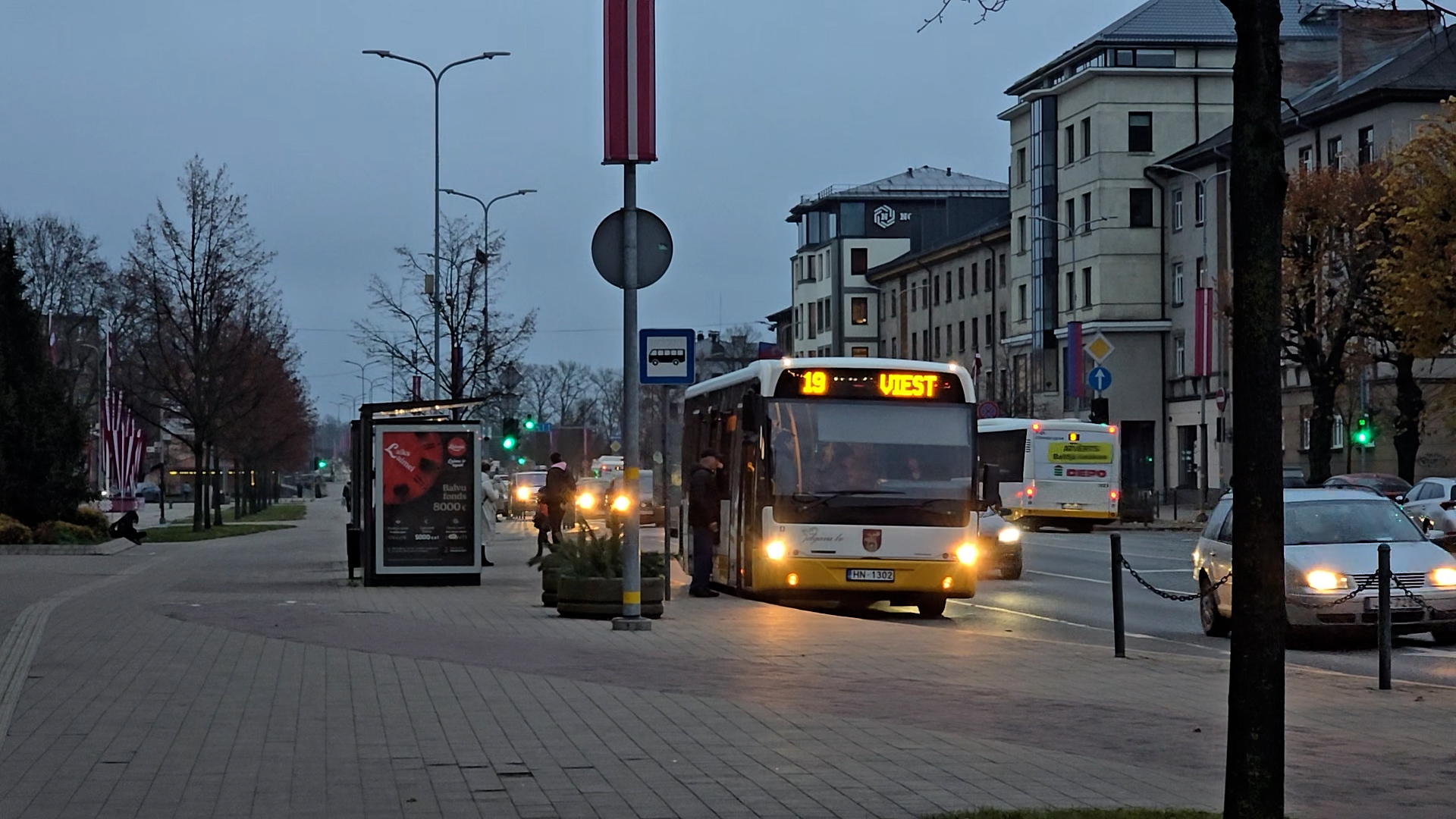 Autobuss pie pieturas Jelgavā agrā rītā ar izgaismotu maršruta numuru.