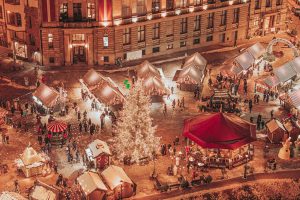 Ziemassvētku tirdziņš Doma laukumā no putna lidojuma ar izgaismotu egli un svētku namiņiem.