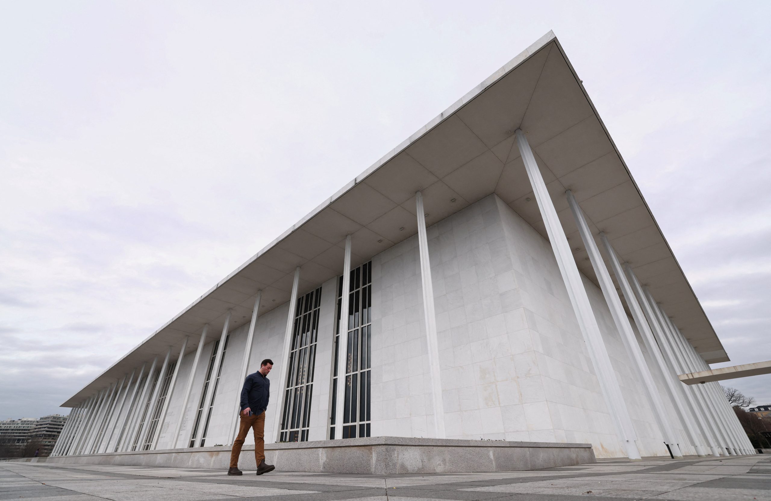 Skats uz Kenedija centra balto, monumentālo ēku Vašingtonā, cilvēks iet garām tās priekšā.
