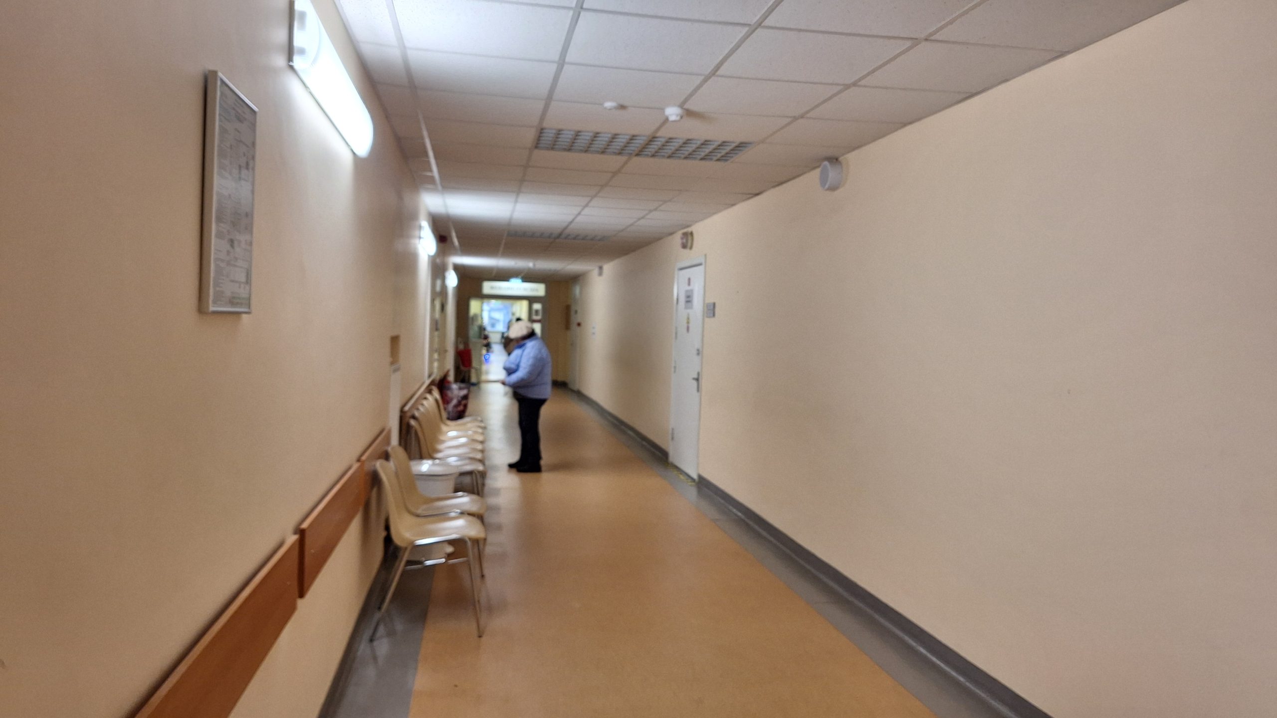 Bauskas slimnīcas gaitenis ar pacientu, ilustrējot veselības aprūpes pieejamību un slimnīcu reformas ietekmi reģionos.