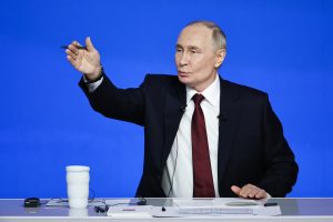 Krievijas prezidents Vladimirs Putins uzstājas preses konferencē pie galda uz zilas fona sienas.
