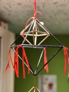 Tradicionāls salmu puzuris ar sarkaniem lentīšu akcentiem, piekārts telpā.