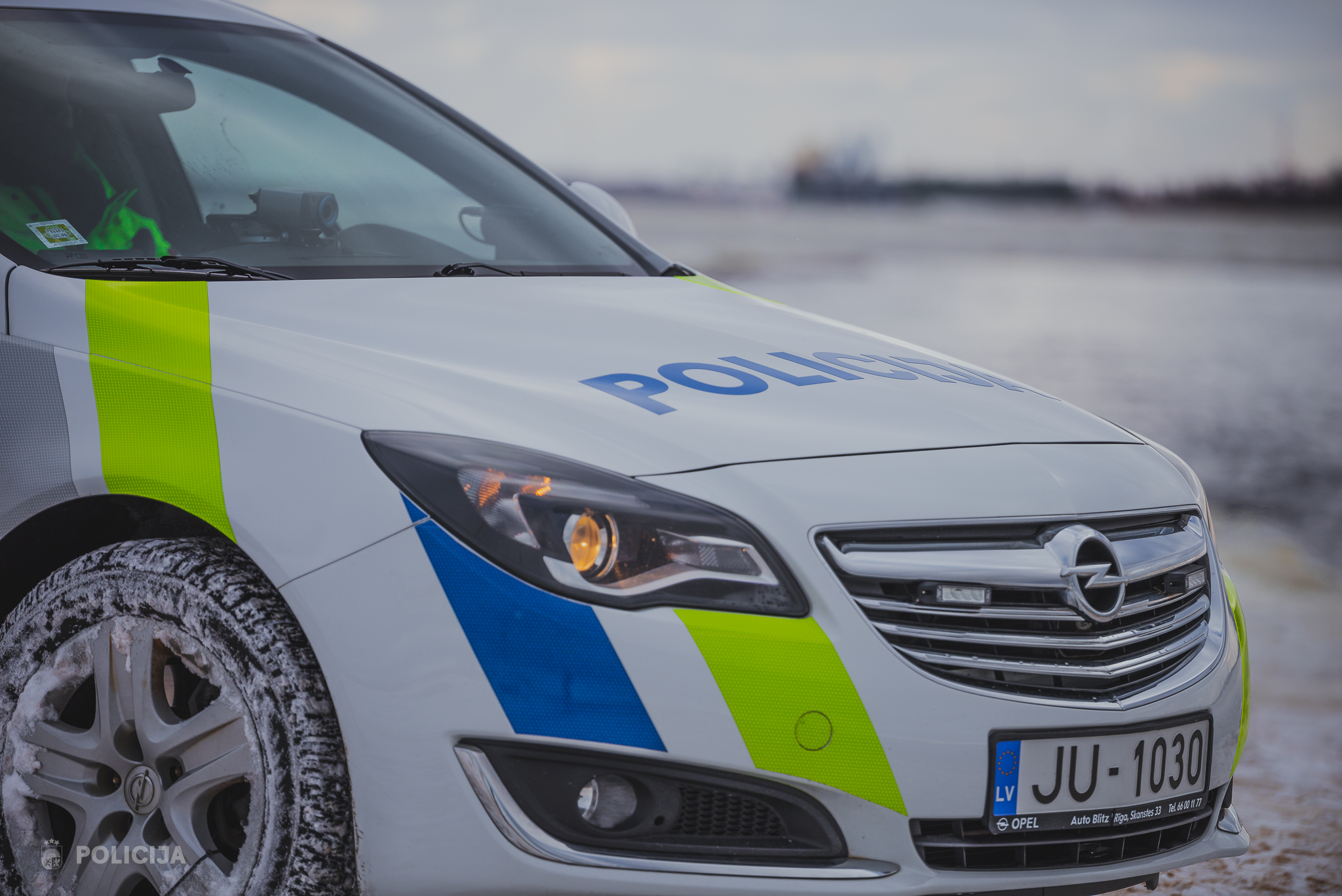 Valsts policijas automašīnas priekšpuse ar sniegu uz riteņa un sāna.