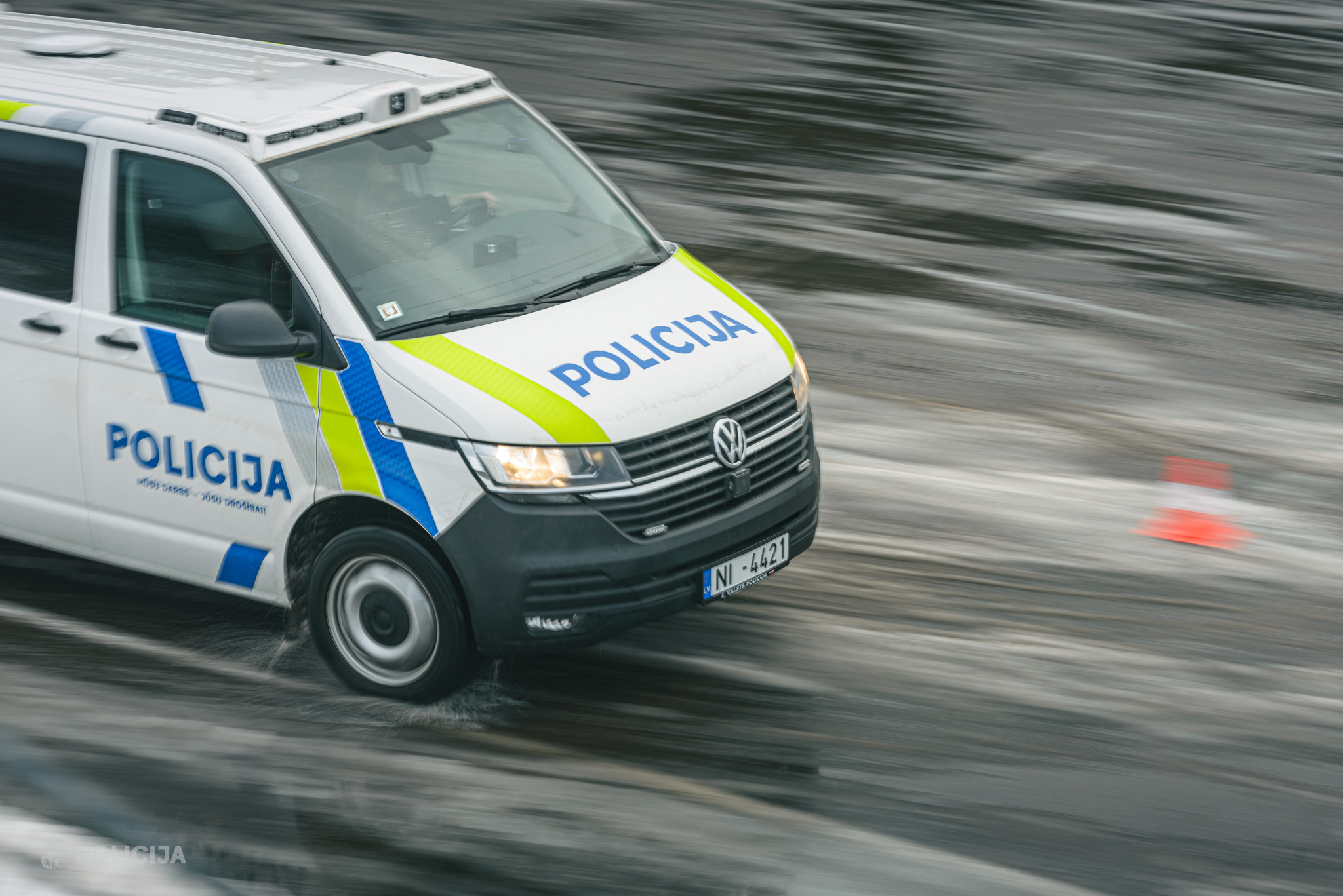 Valsts policijas VW mikroautobuss lielā ātrumā pārvietojas pa slapju asfaltu.