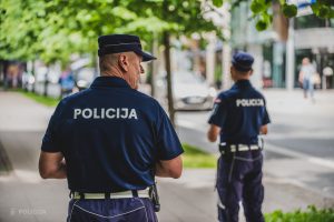 Divi policisti no mugurpuses patrulē pilsētas ielā vasaras dienā.