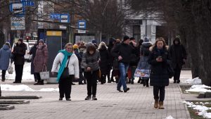 Cilvēki ziemā iet pa pilsētas ietvi pie sabiedriskā transporta pieturas