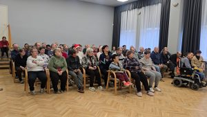 Sociālās aprūpes centra iedzīvotāji sēž zālē un piedalās informatīvā pasākumā par cilvēktiesībām.
