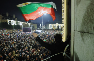 Protestu dalībnieku pūlis Bulgārijā, priekšplānā cilvēks vicina Bulgārijas karogu.