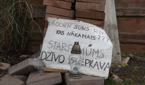 Paštaisīts plakāts un svecīte pie ķieģeļu kaudzes Jēkabpilī.