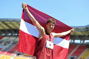 Latvijas jaunais sportists stadionā paceļ Latvijas karogu pēc sacensībām.