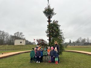Bērni un skolotājas pie rotātas Ziemassvētku egles laukā.