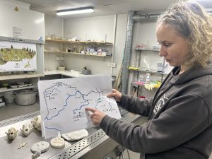 Pētniece laboratorijā rāda arti, kurā ar zīmējumiem atzīmētas lāču uzturēšanās vietas gar upēm.