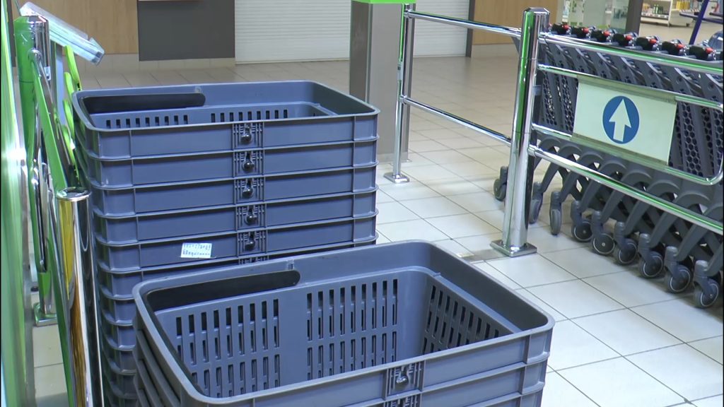 Pelēki plastmasas iepirkumu grozi kaudzē lielveikala ieejas zonā.