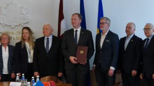 Septiņi cilvēki uzvalkos un lietišķā apģērbā stāv pie karogiem Ekonomikas ministrijā.