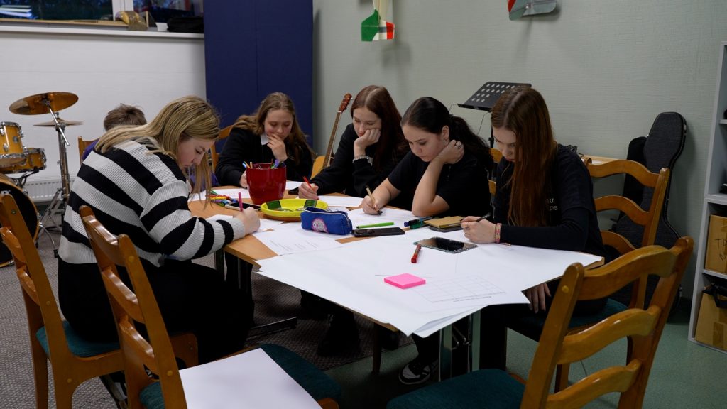 Piecas jaunietes, sēžot pie galda, strādā pie dokumentiem un veic pierakstus forumā "Ko sēsi, to pļausi".