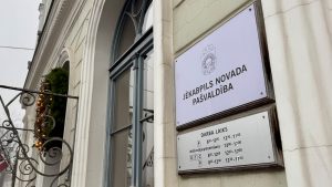 Jēkabpils novada pašvaldības ēkas fasāde ar divām informatīvām plāksnēm par darba laiku un iestādes nosaukumu.