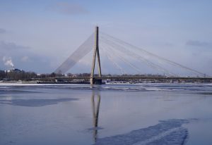 Vanšu tilts Rīgā ziemas dienā, skats pāri Daugavai ar tilta atspulgu ūdenī.