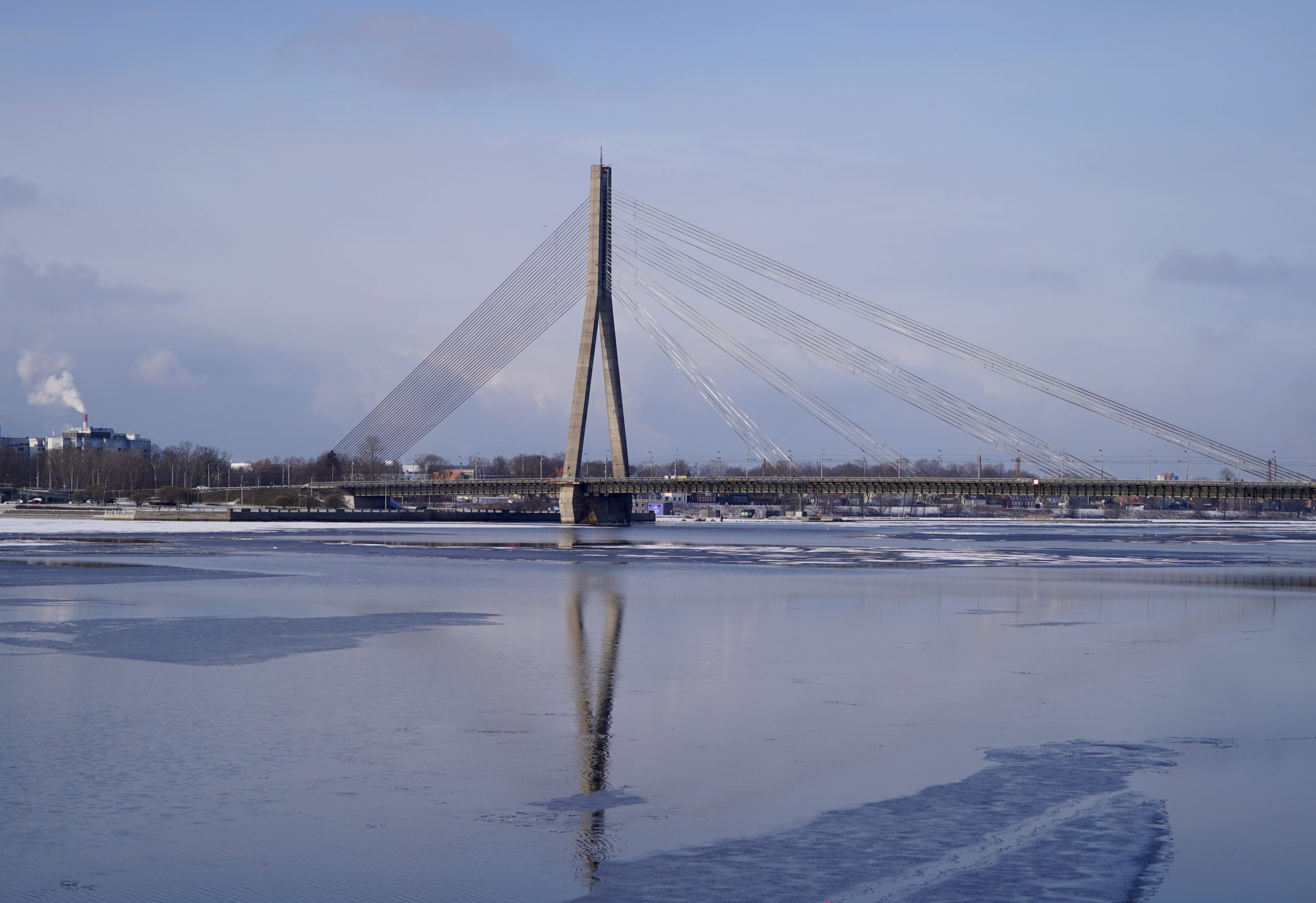 Vanšu tilts Rīgā ziemas dienā, skats pāri Daugavai ar tilta atspulgu ūdenī.