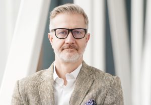 Birokrātijas mazināšanas rīcības grupas vadītājs Jānis Endziņš portreta fotogrāfijā ar brillēm un uzvalka žaketi.