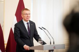 Valsts prezidents Edgars Rinkēvičs uzstājas pie tribīnes ar valsts karogu fonā.