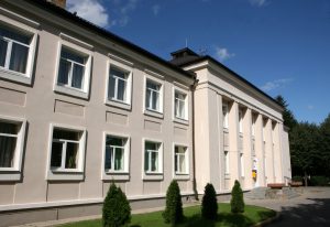 Bauskas slimnīcas ēka ar gaišu fasādi un kolonnām saulainā dienā.