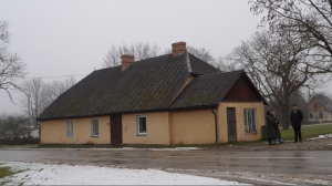vienstāva ēka dzeltenā krāsā ar brūnu jumtu un diviem skursteņiem aukstā, miglainā dienā.