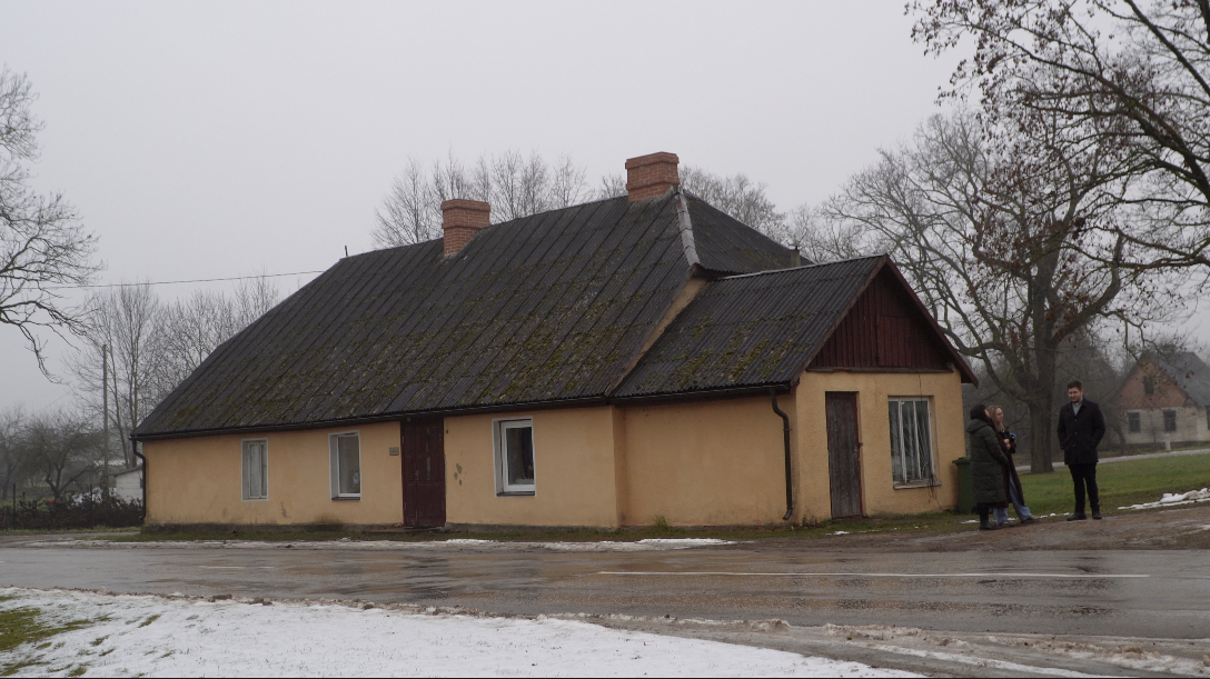 vienstāva ēka dzeltenā krāsā ar brūnu jumtu un diviem skursteņiem aukstā, miglainā dienā.
