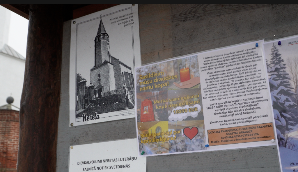 Stends ar melnbaltu baznīcas foto un informāciju par ziedojumu vākšanu apkures maiņai draudzes namā. Nepieciešamā summa 10 390 EUR.