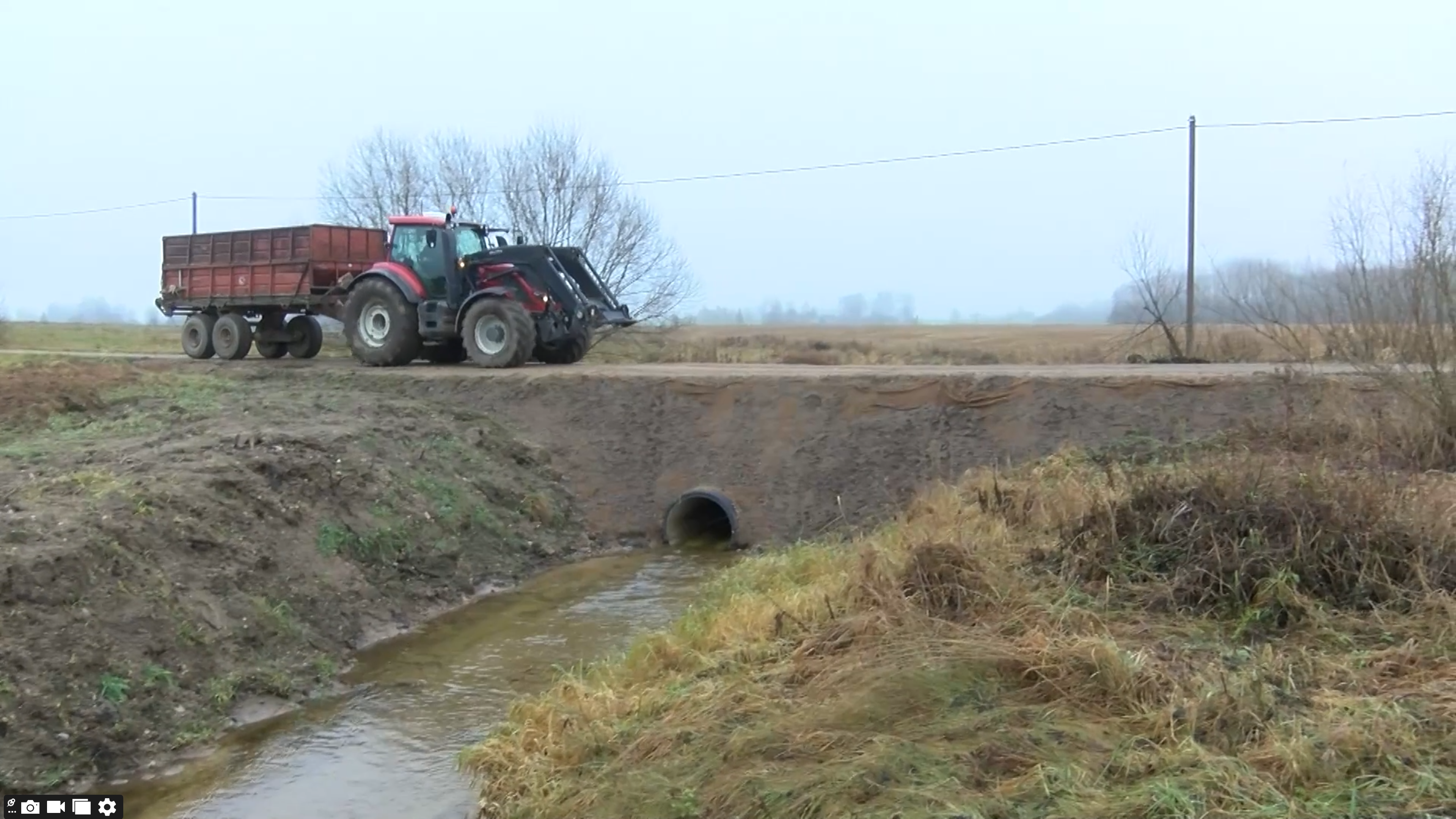 Izskalots ceļa posms Augšdaugavas novadā ar atjaunotu caurteku, pa ceļu brauc traktors pēc vasaras lietavu postījumiem.