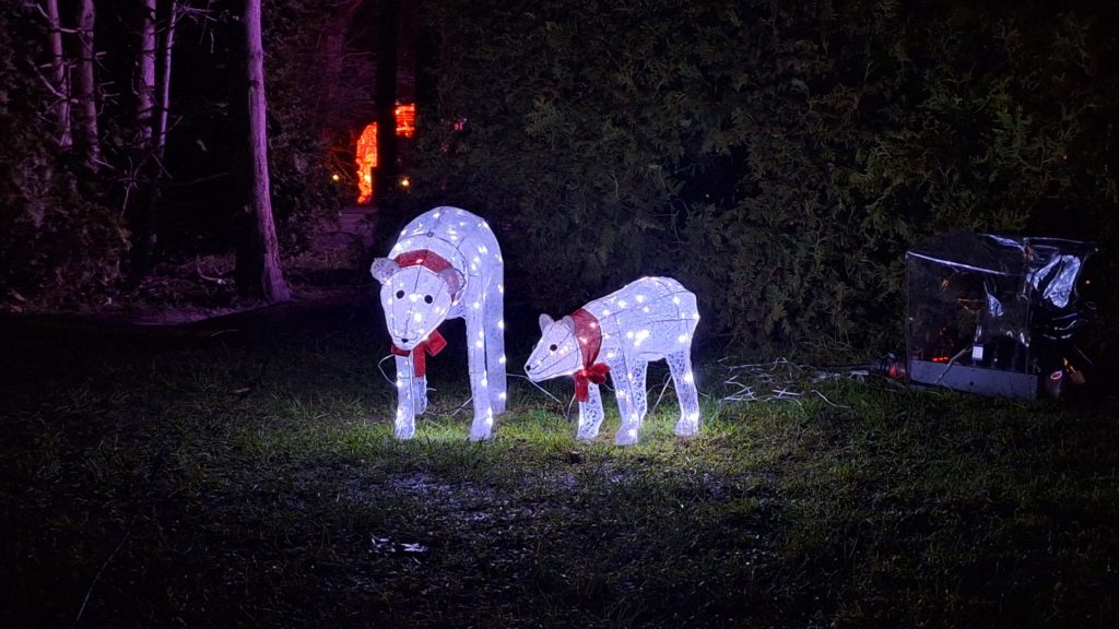 Divi ar LED virtenēm izgaismoti dekoratīvi polārlāči (māte un lācēns) ar sarkanām šallēm stāv uz tumša zāliena.
