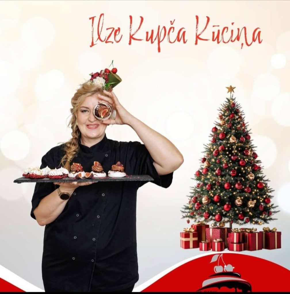 Ilze Kupča Kūciņa melnā pavāra tērpā tur paplāti ar kūciņām pie izrotātas eglītes.