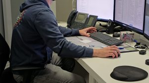 Darbinieks strādā birojā pie datora ar diviem monitoriem.