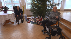 Seniori Ziemassvētkos pansionātā pie eglītes ar saziedotām dāvanām.