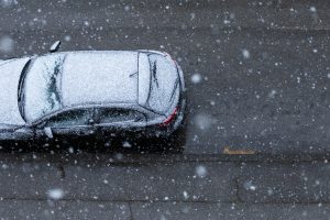 Auto uz ielas, apsnidzis stiprā snigšanā no putna lidojuma skata.