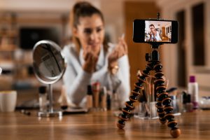 Jauna sieviete filmē grima video sociālajiem tīkliem, izmantojot telefonu uz statīva.
