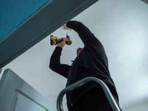 Meistars uzstāda dūmu detektoru pie griestiem, izmantojot elektrisko skrūvgriezi