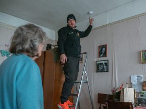 Meistars uz kāpnēm uzstāda dūmu detektoru seniora dzīvoklī