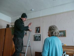Meistars uz kāpnēm skaidro dūmu detektora darbību iedzīvotājai dzīvoklī