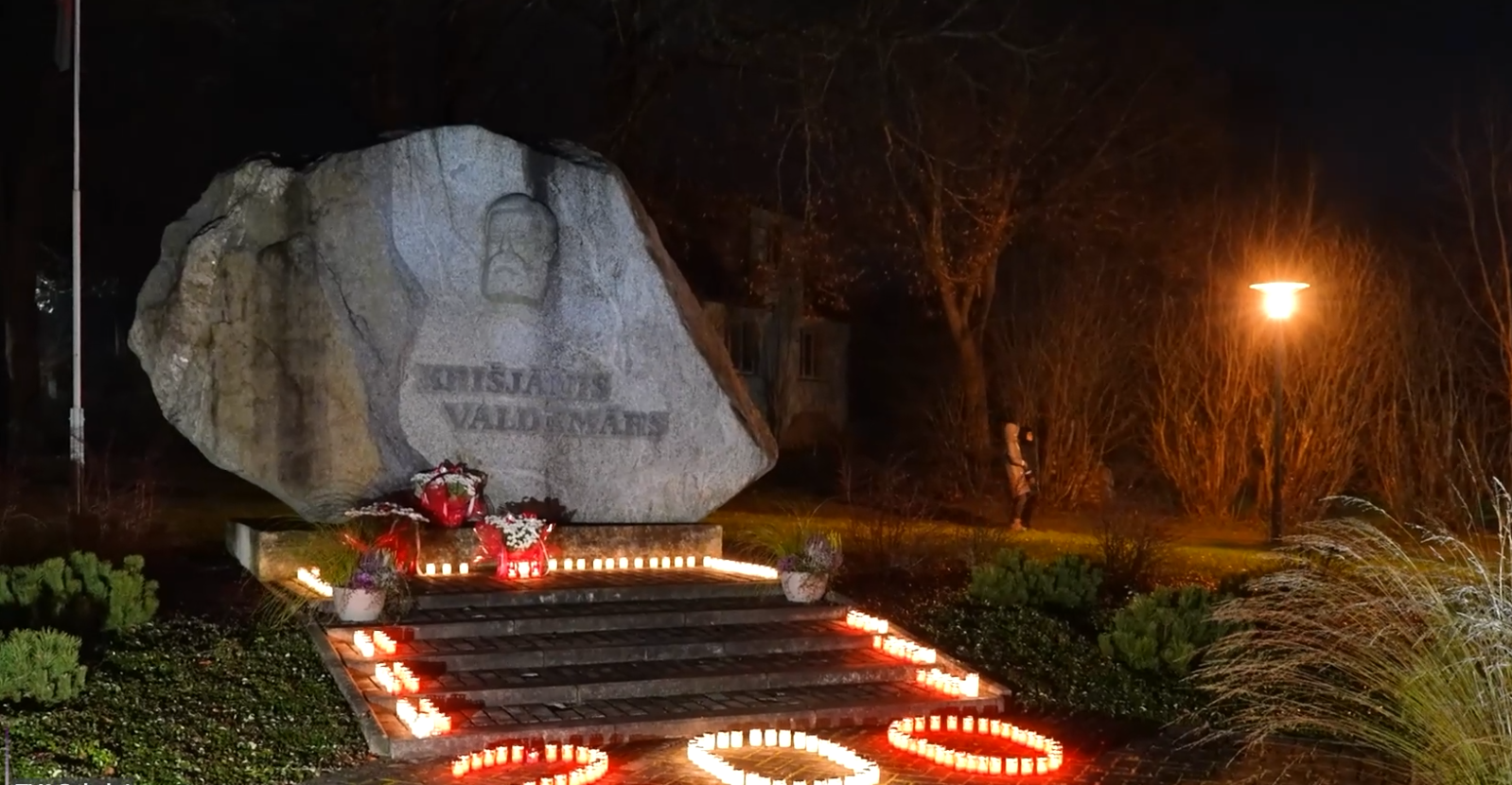 Liels, gaišpelēks laukakmens ar Krišjāņa Valdemāra bareljefu un uzrakstu, kas aptverts ar svecīšu gaismām tumsā.