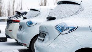 Ar sniegu klāti elektroauto, kas novietoti stāvvietā ziemas apstākļos.