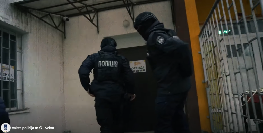 Ukrainas policijas darbinieki maskās un specapģērbā dodas iekšā ēkā kratīšanas laikā.